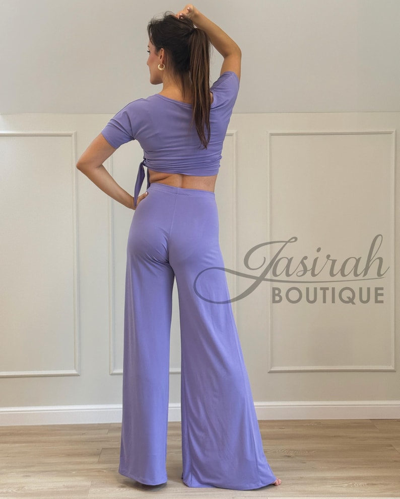 May include: A lavender two-piece outfit featuring a short-sleeved crop top with a tie closure and wide-leg pants. The outfit is made of a soft, flowing fabric. The text "Jasirah Boutique" is visible in the lower right corner.
