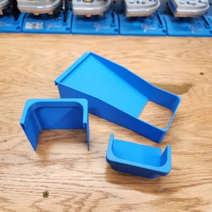 May include: Three blue plastic parts for a 3D printed project. The parts are shaped like a ramp, a U-shaped piece, and a smaller U-shaped piece.