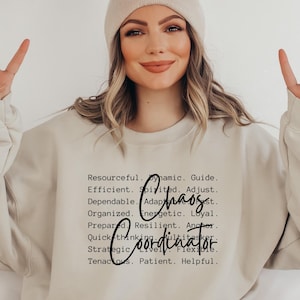 Może przedstawiać: Beżowa bluza z napisem "Coordinator" w ozdobnej czcionce, z napisem "Chaos" nad nim. Bluza ma również listę słów opisujących cechy koordynatora. Osoba na zdjęciu ma na sobie beżową czapkę.