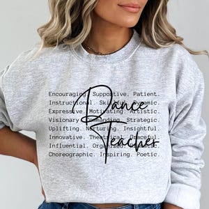 May include: Gray sweatshirt with the text "Dance Teacher" in black cursive lettering. The text is surrounded by a list of positive adjectives describing a dance teacher.