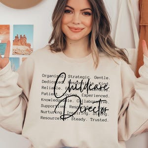 May include: A beige sweatshirt featuring the words "Childcare Director" in a black script font. The sweatshirt also lists positive attributes such as "Organised", "Dedicated", and "Reliable".