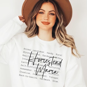 May include: White sweatshirt with black text that reads "Homestead Mama" and a list of words describing the lifestyle, including "Animal caretaker", "Handy", "Rural", "Strong-willed", "Gardener", "DIYer", "Resilient", "Resourceful", "Baking", "Intentional", "Patient", "Homemade", "Earthy", "Sustainable", "Nurturing", "Self-sufficient", "Preserver", "Holistic", "Homemaker", "Independent", "Forager", "Back-to-basics", "Hardwork", "Grow".