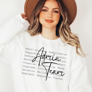 May include: White long-sleeved sweatshirt with the words "Admin Team" in a black script font. The sweatshirt also features a list of descriptive words in a black font, such as "Detail-oriented" and "Communicative".