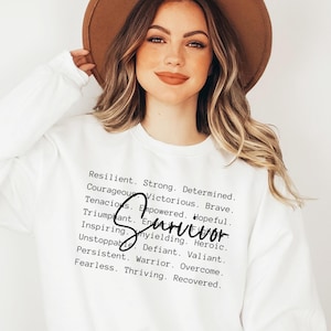 May include: White sweatshirt with the word "SURVIVOR" written in black cursive. The text "Resilient. Strong. Determined. Courageous. Victorious. Brave. Tenacious. Empowered. Hopeful. Triumphant. Unyielding. Heroic. Inspiring. Defiant. Valiant. Unstoppable. Warrior. Overcome. Persistent. Thriving. Recovered." is printed in black below the word "SURVIVOR".