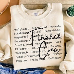 May include: Cream-colored sweatshirt with the words "Finance Crew" in black script. The sweatshirt has a crew neck and long sleeves. The words "Analytical, Methodical, Honest" are printed on the shirt.