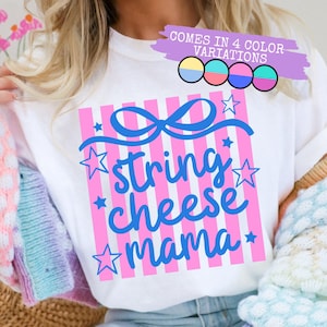 Könnte beinhalten: Weißes T-Shirt mit einem rosa-weiß gestreiften Design. Das Shirt zeigt den Text "string cheese mama" in blauer Schrift, mit einer Schleife und Sternen. Das Bild zeigt auch den Text "COMES IN 4 COLOR VARIATIONS".