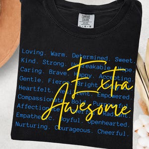 May include: Black t-shirt with the words "Extra Awesome" in yellow script. The shirt also features a list of positive adjectives in blue font, including "Loving," "Kind," and "Brave."