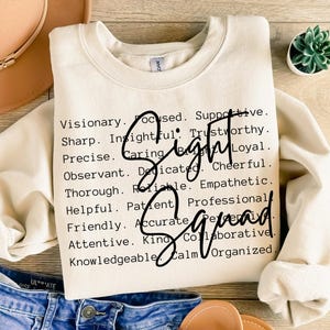 May include: Cream-colored sweatshirt with the words "Sight Squad" in a black script font. The sweatshirt has a crew neck and long sleeves. The words "Visionary, Focused, Supportive, Sharp, Insightful, Trustworthy" are printed in a black font.