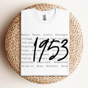 May include: White t-shirt with the number "1953" in a bold, handwritten style. The shirt features a list of words such as "Retro," "Vintage," and "Historic." The shirt is displayed on a woven, circular surface.