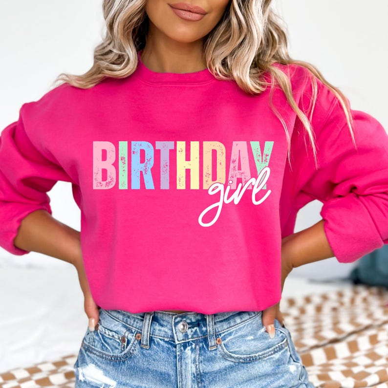 Może przedstawiać: Jasnor&oacute;żowa bluza z napisem "BIRTHDAY girl". Słowo "BIRTHDAY" jest w stylu blokowym z pastelowymi kolorami, a "girl" jest w kursywie. Modelka ma na sobie niebieskie dżinsowe szorty.