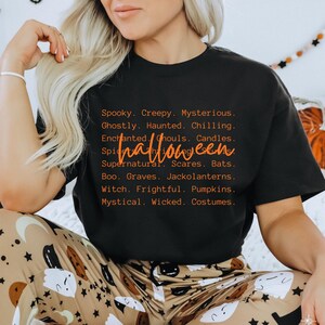 May include: Black t-shirt with orange text that reads "Halloween" and a list of spooky words. The shirt is part of a Halloween-themed collection. The model is wearing patterned pajama pants.