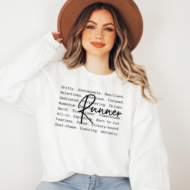 May include: White sweatshirt with a black text graphic that reads "Gritty. Unstoppable. Resilient. Relentless. Zenacious. Focused. Dedicated. Persevering. Driven. Momentum. Runner Swift. Trailblazer. Powerhouse. All-in. Explosive. Born to run. Fearless. Paced. Victory-bound. Goal-chase. Enduring. Athletic."