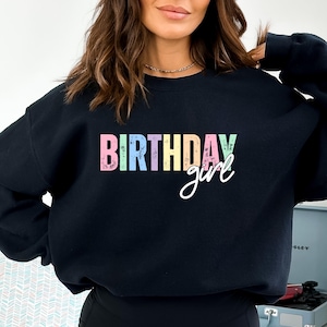 Może przedstawiać: Czarna bluza z napisem "BIRTHDAY girl" w pastelowych literach. Słowo "BIRTHDAY" jest w bloku, a "girl" jest kursywą. Bluza ma okrągły dekolt.