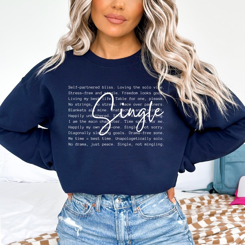 May include: A navy blue sweatshirt with white text that reads "Self-partnered bliss. Loving the solo vibe. Stress-free and single. Freedom looks good. Living my best life. Table for one, please. No strings, no stress. Peace over partners. Blankets all mine. Unattached and single. Happily unbothered. Single hot sorry. I am the main character. Time spent for me. Happily my own. Single not sorry. Diagonally sleeping goals. Drama-free zone. Me time = best time. Unapologetically solo. No drama, just peace. Single, not mingling."