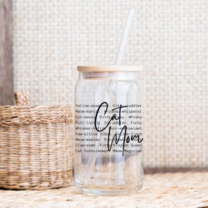 May include: A clear glass tumbler with a bamboo lid and a straw. The tumbler has the words "Cat Mom" in a black script font, along with a list of cat-related words. A woven basket is in the background.