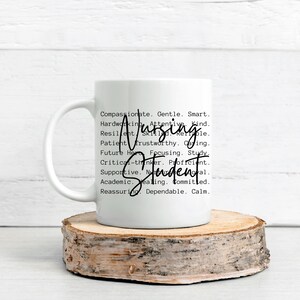 May include: White ceramic mug with a black handle. The mug has a black graphic that says "Nursing Student" and lists a variety of positive adjectives describing a nursing student.