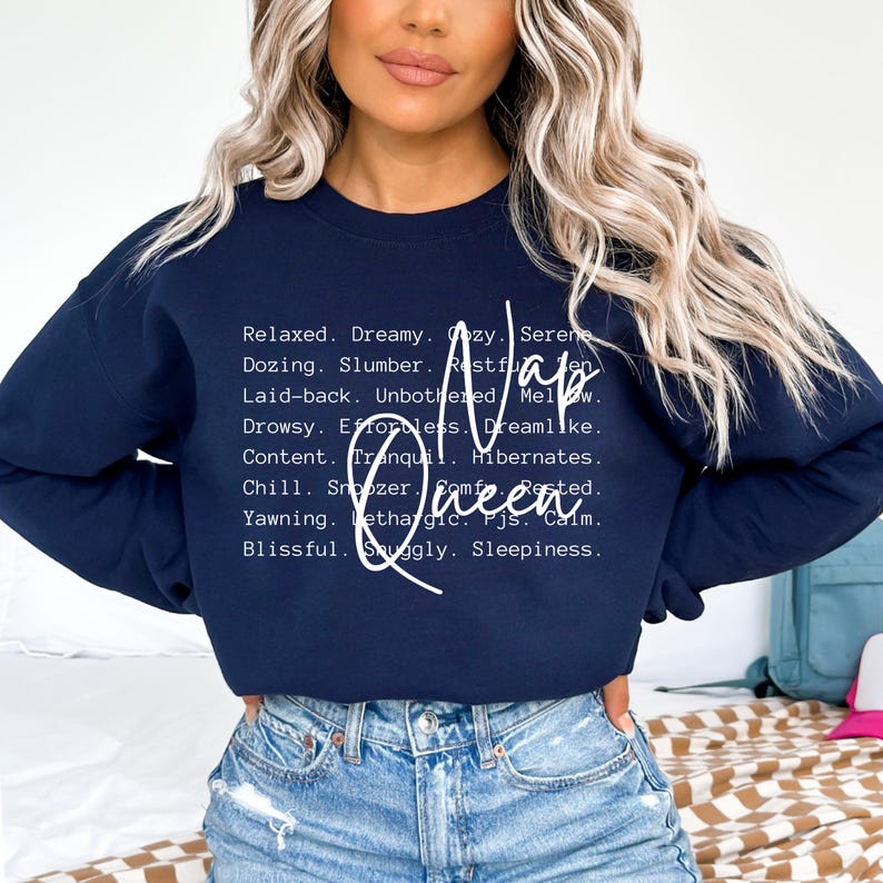 以下が含まれることがあります： 「Nap Queen」と白文字で書かれたネイビーブルーのスウェットシャツ。リラックス、夢、居心地の良さ、穏やか、うたた寝、睡眠、休息、気楽、気楽、穏やか、眠い、努力なし、夢のような、満足、静か、冬眠、リラックス、居眠り、快適、休んだ、あくび、無気力、パジャマ、穏やか、幸せ、心地よい、眠気など、昼寝に関連する単語がリストされています。