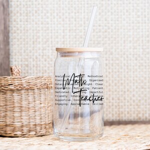 May include: A clear glass tumbler with a wooden lid and a straw. The tumbler has a black graphic that says "Math Teacher" and lists positive attributes of a math teacher.