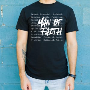 Op de afbeelding: Zwart t-shirt met de witte tekst "MAN OF FAITH" en een lijst met deugden. Dit casual kledingstuk is gemaakt van een comfortabele stof.