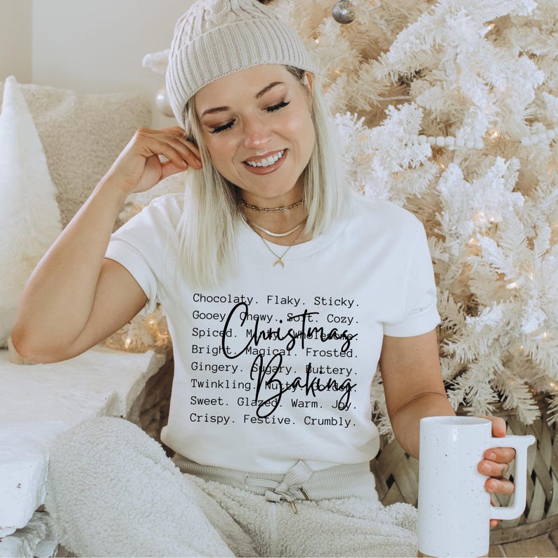 Pu&ograve; includere: Una t-shirt bianca a maniche corte con testo nero che recita: Chocolaty. Flaky. Sticky. Gooey. Chewy. Soft. Cozy. Spiced. Magical. Frosted. Gingery. Sugary. Buttery. Twinkling. Nutty. Sweet. Glazed. Warm. Joy. Crispy. Festive. Crumbly. Christmas Baking.