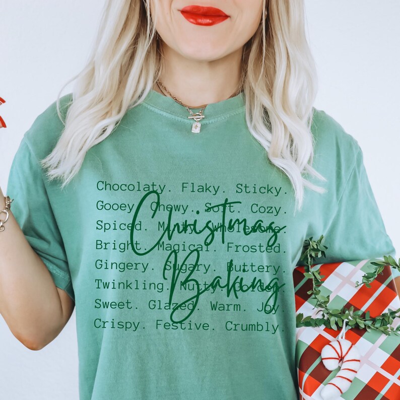 Pu&ograve; includere: Una t-shirt a maniche corte color verde salvia con testo stampato in nero che elenca vari aggettivi come Chocolaty, Flaky, Sticky e altri, con la scritta in corsivo verde scuro Christmas Baking sovrapposta al centro della t-shirt.