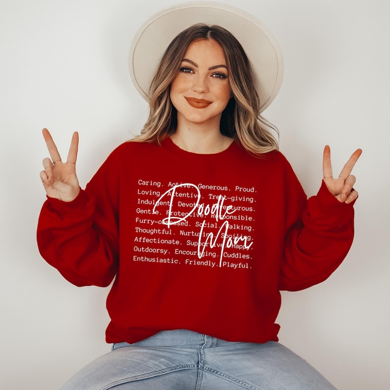 May include: Red sweatshirt with white text that reads "Doodle Mom" and a definition of the word "Doodle Mom" including words like caring, active, generous, proud, loving, attentive, and playful.