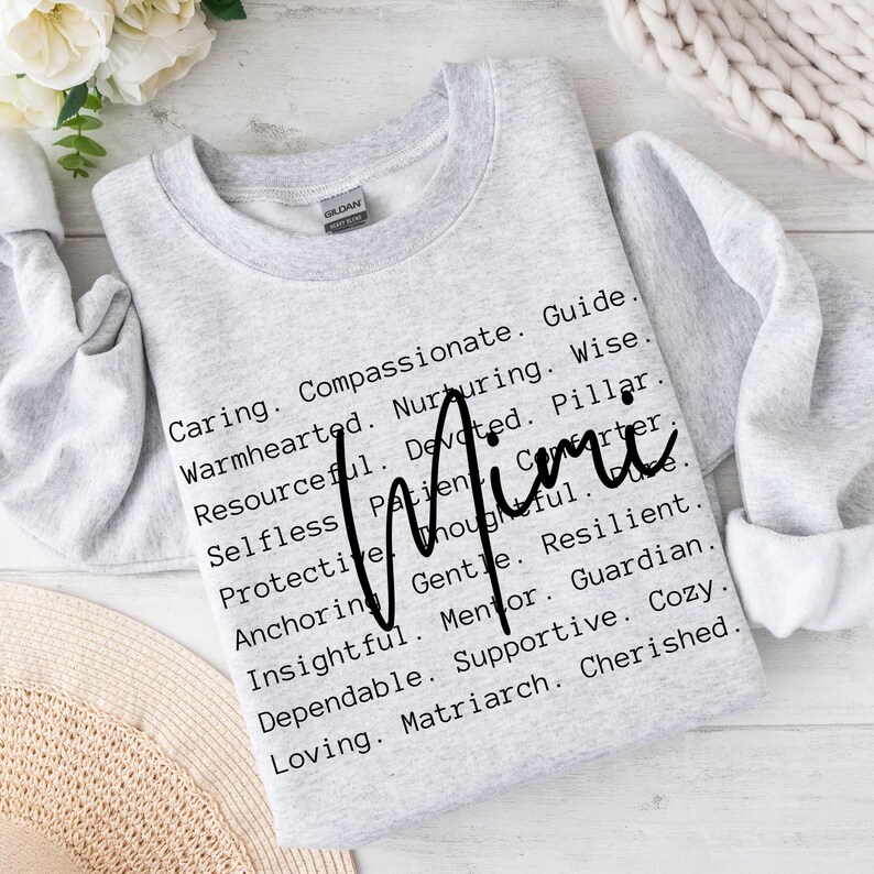 May include: Grey sweatshirt with the word "Mimi" written in black cursive. The text below the name lists positive attributes such as caring, compassionate, guide, warmhearted, nurturing, wise, resourceful, devoted, pillar, selfless, patient, thoughtful, gentle, resilient, anchoring, mentor, guardian, insightful, dependable, supportive, cosy, loving, and matriarch.