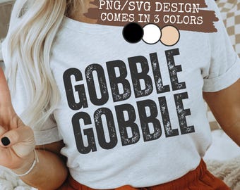 May include: A light gray t-shirt with the words "GOBBLE GOBBLE" in distressed black lettering. The top text reads "PNG/SVG DESIGN COMES IN 3 COLORS" with color options. The model is wearing orange shorts.