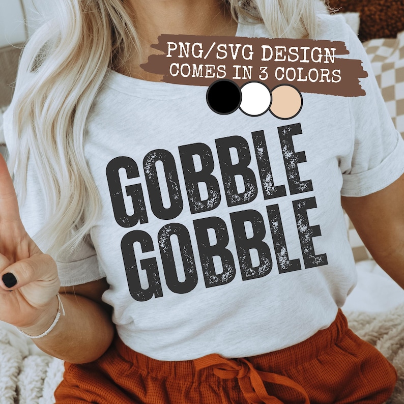 May include: A light gray t-shirt with the words "GOBBLE GOBBLE" in distressed black lettering. The top text reads "PNG/SVG DESIGN COMES IN 3 COLORS" with color options. The model is wearing orange shorts.