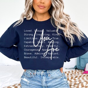 May include: Navy blue sweatshirt with white text that reads "You Are" and a list of positive attributes, including loved, enough, valuable, strong, inspiring, kind, limitless, true, capable, smart, amazing, extraordinary, powerful, courageous, appreciated, brave, admired, radiant, beautiful, and incomparable.