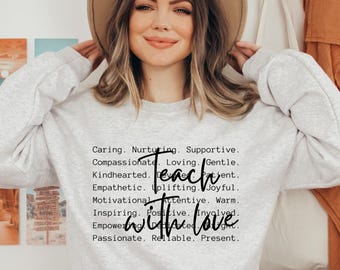 Może przedstawiać: Jasnoszara bluza z okrągłym dekoltem i czarnym napisem: Caring. Nurturing. Supportive. Compassionate. Loving. Gentle. Kindhearted. Devoted. Patient. Empathetic. Uplifting. Joyful. Motivational. Attentive. Warm. Inspiring. Positive. Involved. Empowering. Dedicated. Bright. Passionate. Reliable. Present. Teach with love.