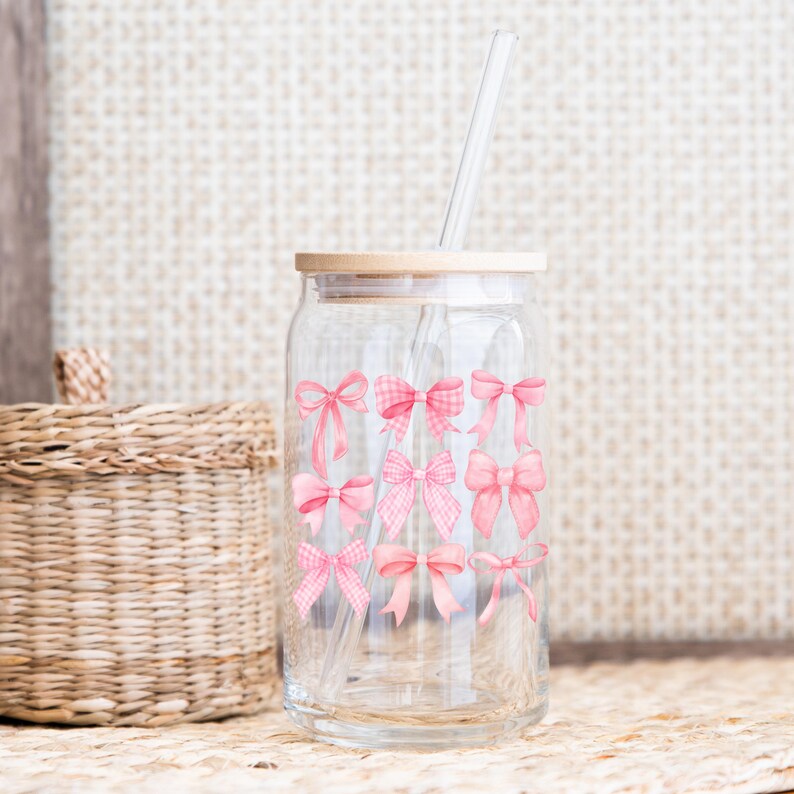 Puede incluir: Un tarro de vidrio transparente con tapa de madera y pajita transparente. El tarro est&aacute; decorado con lazos rosas de varios dise&ntilde;os. Una cesta de mimbre est&aacute; en el fondo.