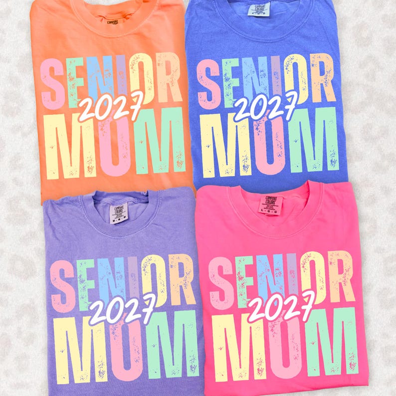 Puede incluir: Cuatro camisetas coloridas en naranja, azul, morado y rosa. Cada camiseta presenta el texto "SENIOR 2027 MUM" en una fuente multicolor desgastada. Las camisetas son probablemente de algod&oacute;n y de estilo casual.