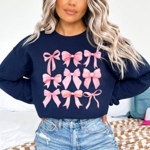 Puede incluir: Sudadera azul marino con un estampado de nueve lazos rosas de varios estilos. Algunos lazos tienen un dise&ntilde;o de cuadros. La sudadera es de cuello redondo y est&aacute; hecha de un material suave. Los lazos tienen un efecto acuarela.