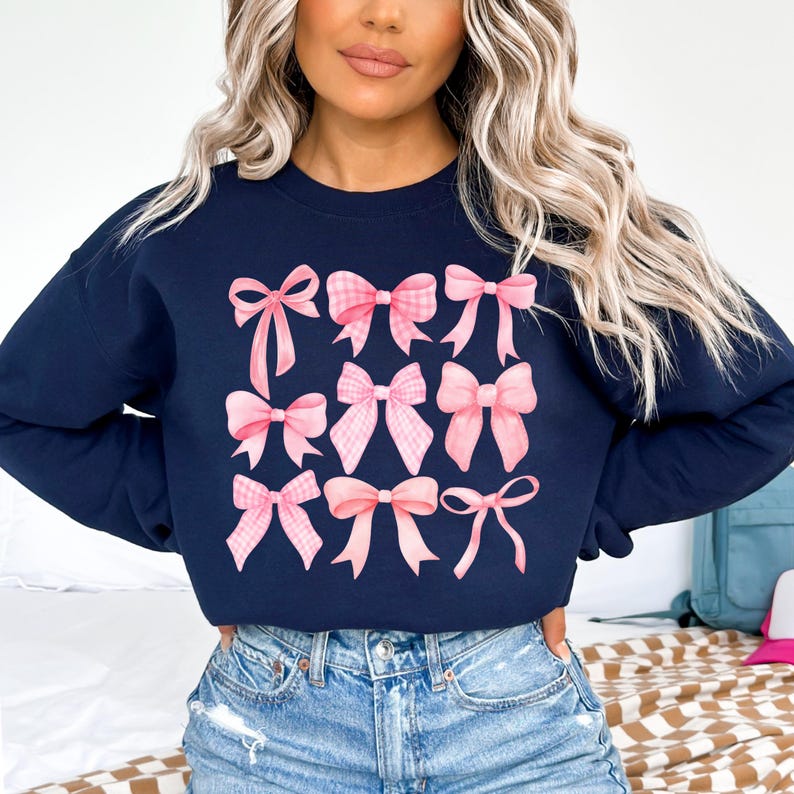 Puede incluir: Sudadera azul marino con un estampado de nueve lazos rosas de varios estilos. Algunos lazos tienen un dise&ntilde;o de cuadros. La sudadera es de cuello redondo y est&aacute; hecha de un material suave. Los lazos tienen un efecto acuarela.
