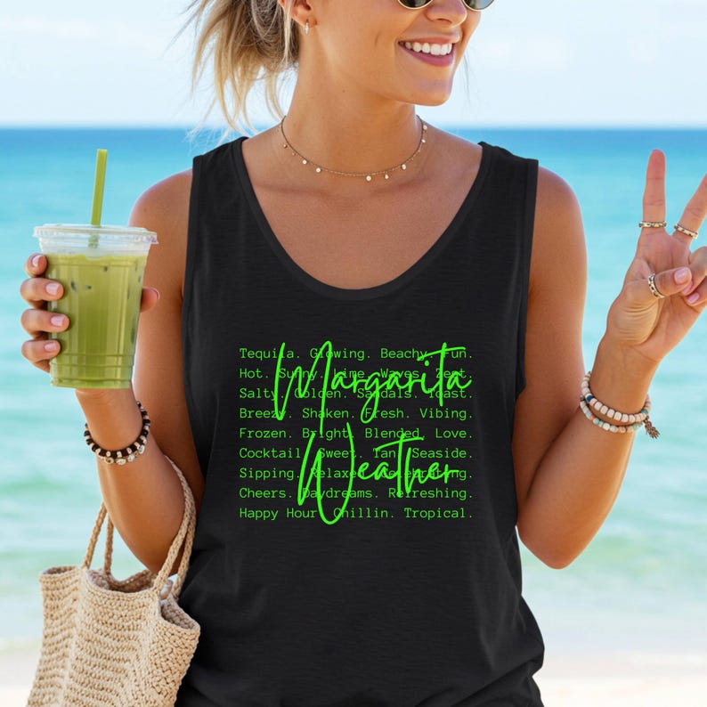 May include: Black tank top with the words "Margarita Weather" in green script. The tank top is worn by a person holding a green drink in a clear plastic cup. The background is a beach scene with blue water and sky.