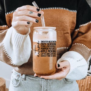 K&ouml;nnte beinhalten: Ein klares Glas mit Holzdeckel und Glasstrohhalm, gef&uuml;llt mit einem cremigen Getr&auml;nk. Auf dem Glas steht das Wort "Autumn" in Schrift und der Text "Sweater Weather, Cozy Season, Pumpkin Patches, Apple Picking, Lattes and Layers".