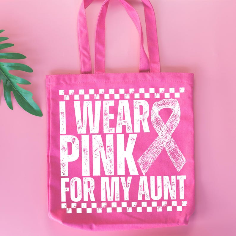 May include: A pink tote bag with white text that reads "I WEAR PINK FOR MY AUNT" and a white ribbon graphic. The bag has two handles and is set against a pink background with a green leaf.
