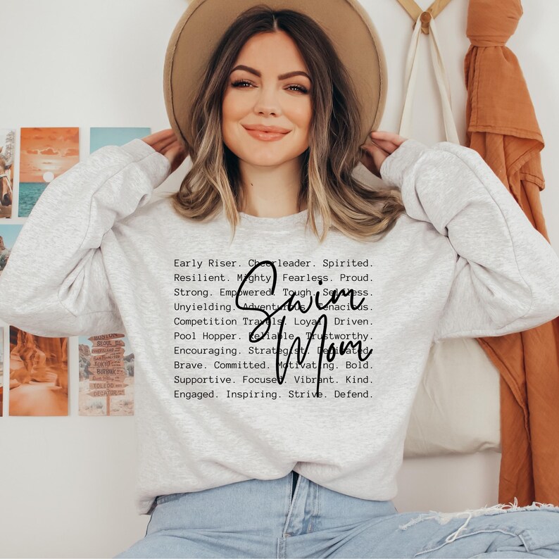 May include: A gray sweatshirt with the text "Early Riser. Cheerleader. Spirited. Resilient. Mighty. Fearless. Proud. Strong. Empowered. Tough. Seamless. Unyielding. Adventurous. Tenacious. Competition Trails. Loyal. Driven. Pool Hopper. Reliable. Trustworthy. Encouraging. Strategic.  Battle-Tested. Brave. Committed. Motivating. Bold. Supportive. Focused. Vibrant. Kind. Engaged. Inspiring. Strive. Defend." and the word "Swim Mom" in large, bold letters.