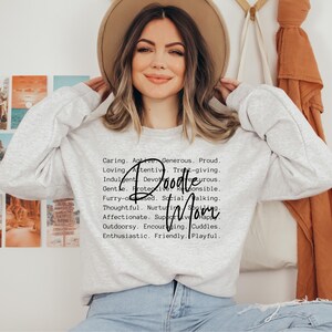 May include: A gray sweatshirt with the text "Doodle Mom" in black cursive lettering. The text is surrounded by a list of positive adjectives describing a mother.