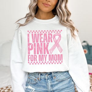 May include: White sweatshirt with the text "I Wear Pink For My Mom" in pink, along with a pink ribbon graphic. The sweatshirt has a crew neck and long sleeves. The text is in a distressed font.