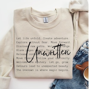 May include: A beige sweatshirt with a black text print that reads "Let life unfold. Create adventure. Explore without fear. Move forward. Discover new paths. Welcome change. Blank pages await. Trust the blank. Release control. Let life surprise. Move freely. Follow your curiosity. Welcome the mystery. Let go, grow. Detours lead to unexpected beauty. The Unknown is where magic begins."