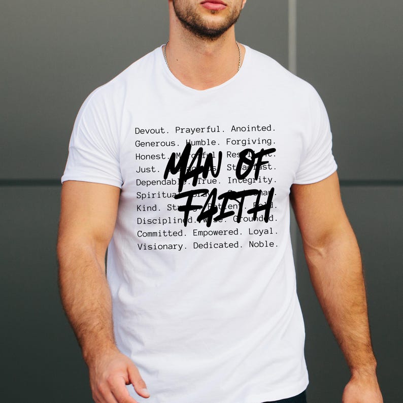 Op de afbeelding: Wit T-shirt met de woorden "MAN OF FAITH" in een gedurfde, handgeschreven stijl. Het shirt heeft ook een lijst met positieve eigenschappen in een kleinere, gedrukte letter, waaronder woorden als "Devout", "Honest" en "Committed".