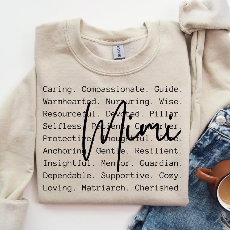 May include: A beige sweatshirt with the words "Caring. Compassionate. Guide. Warmhearted. Nurturing. Wise. Resourceful. Devoted. Pillar. Selfless. Patient. Comforter. Protective. Thoughtful. True. Anchoring. Gentle. Resilient. Insightful. Mentor. Guardian. Dependable. Supportive. Cozy. Loving. Matriarch. Cherished." printed in black.