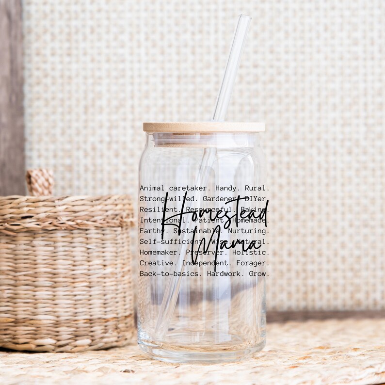 May include: A clear glass jar with a wooden lid and a straw. The jar has a black and white design with the text "Homestead Mama" and a list of words describing the lifestyle.