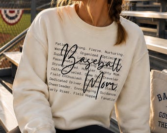 May include: A cream-colored crewneck sweatshirt featuring black text that lists various descriptive words like Patient, Strong, Fierce, Nurturing, and more, with the words Baseball Mom written in a large, black, cursive script overlaying the text.