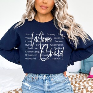 May include: Navy blue sweatshirt with white text that reads "Moon Child" and a list of words describing the moon, such as "dreamy", "glow", "serene", "mysterious", "artistic", "whimsical", and "luminous".