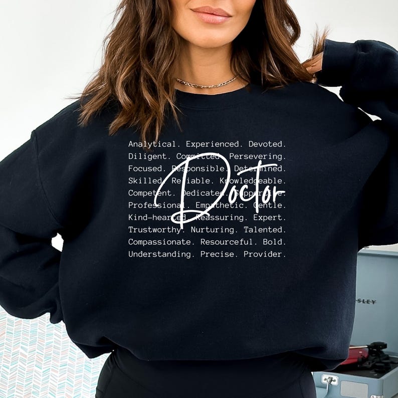 May include: Black sweatshirt with white text that reads "Doctor" and a list of positive attributes associated with the profession.