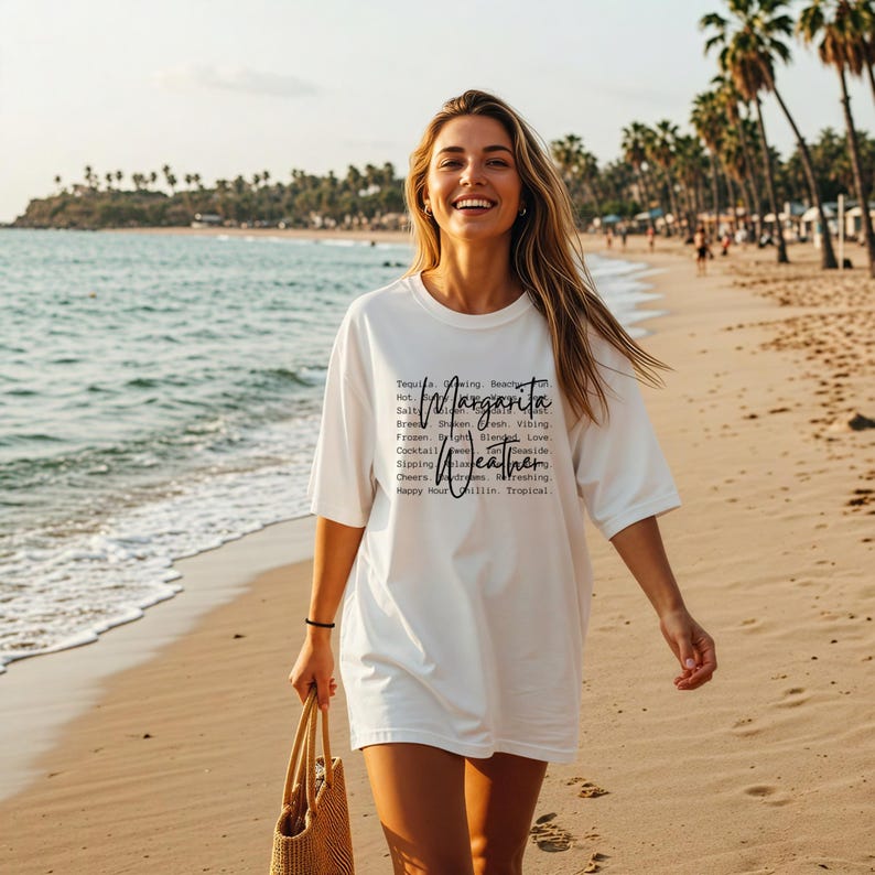 May include: A white t-shirt with the words "Margarita Weather" printed on it. The shirt is worn by a person walking on a sandy beach. The text includes words like "Tequila", "Salty", "Frozen", "Cocktail", "Sipping", "Cheers", and "Happy Hour".