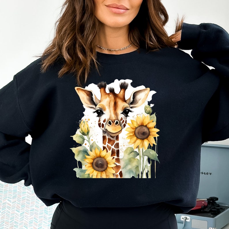 May include: Black sweatshirt featuring a watercolour illustration of a giraffe with sunflowers. The giraffe is looking at the viewer with its head tilted slightly to the side.